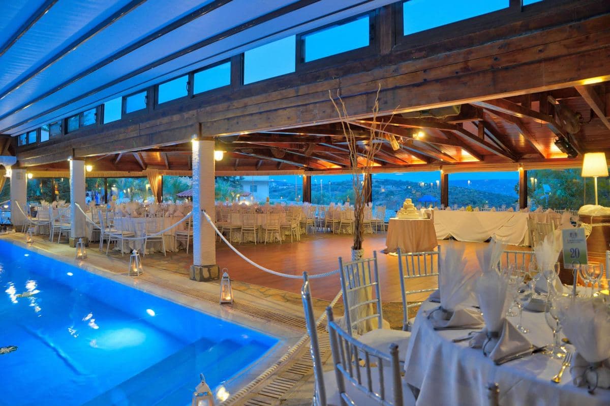 Reception hall with set tables and pool at twilight — Ktima Filokalis wedding venue Koropi